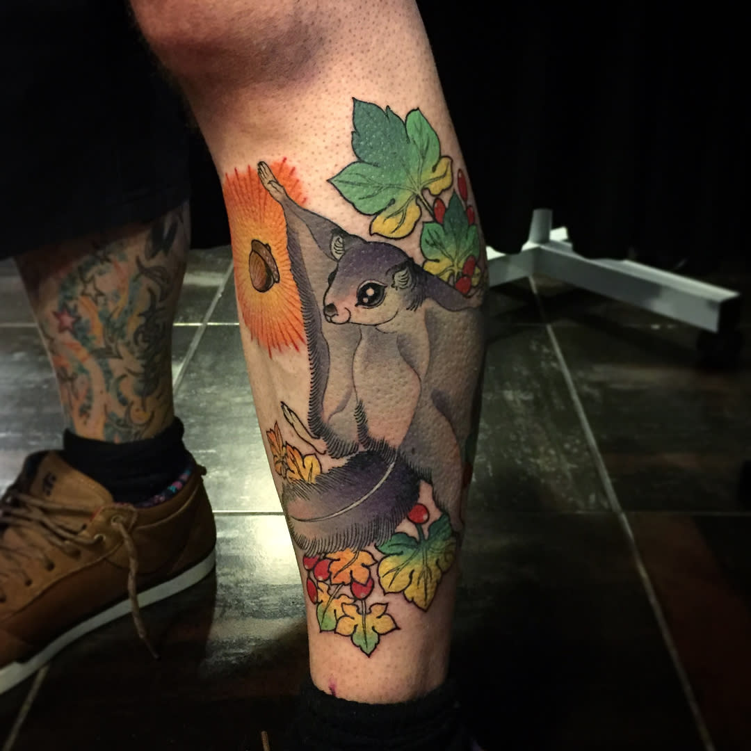Colorful flying squirrel tattoo on a man's calf, surrounded by leaves and an acorn